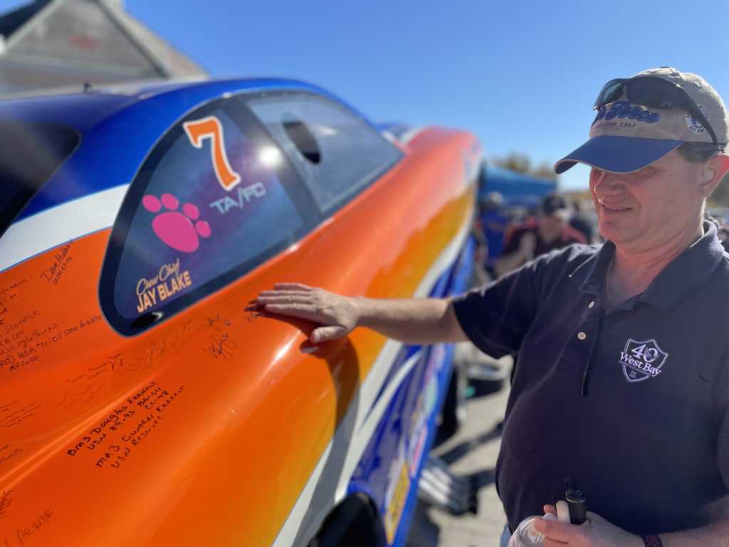 A man wearing a baseball hat and a blue shirt runs his hand over the side of the Follow A Dream funny car.