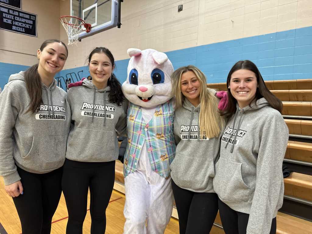 Four Providence College Cheerleaders standing with the Easter Bunny looking at the camera.