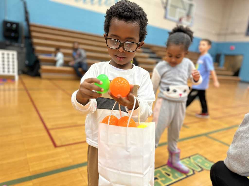 A young boy wearing black-rimmed glasses holds a bag full of colorful eggs.
