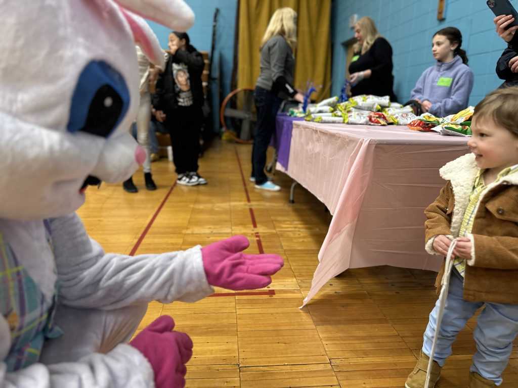 A young boy wearing a brown coat and blue pants looks at the Easter Bunny.