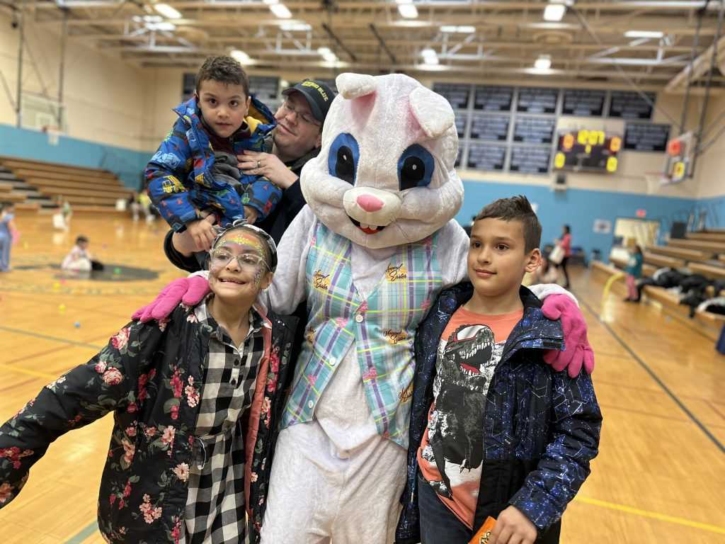 Three young kids, one being held by a man, pose with the Easter Bunny.