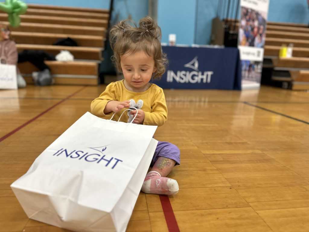 A young girl sits on the floor with a large white paper bag with the INSIGHT logo printed on it.
